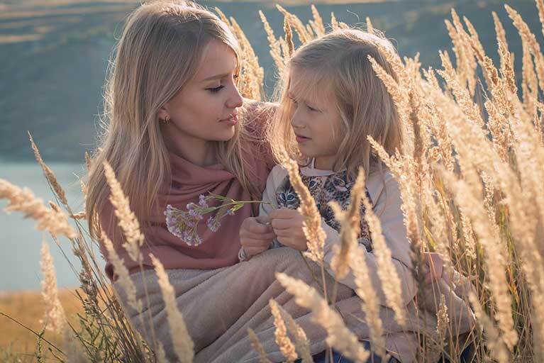 Mutter kniet neben Kind im Gras: Kopfläuse bei Erwachsenen