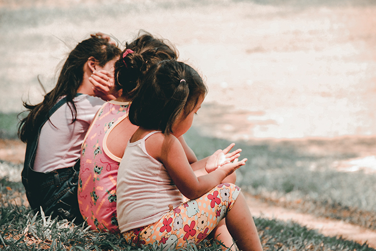 3 Kinder sitzen am Wiesenrand